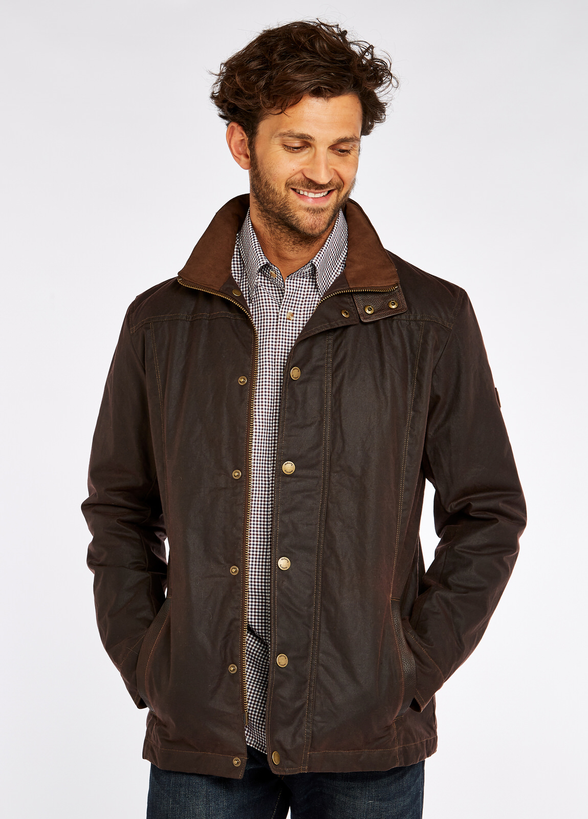 Waist up view of a male model wearing a java brown coloured Dubarry Carrickfergus waxed jacket, open with the lighter brown inside collar visible. The model is also wearing a white and black checkered shirt