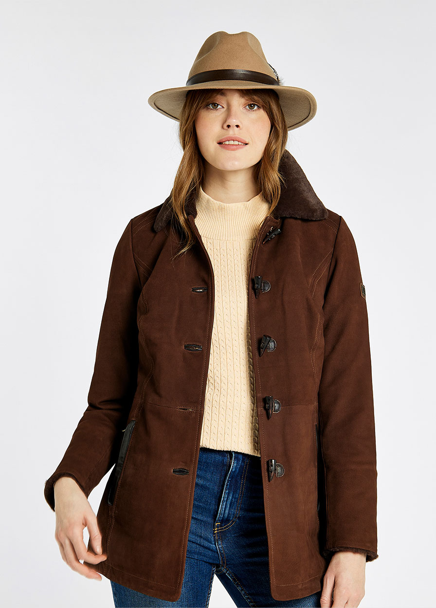 Model wearing a women's Dubarry Clarke leather jacket opened, the walnut brown coloured jacket has a fur collar and toggle buttons. The model is also wearing a beige hat, a cream jumper, blue jeans and brown boots