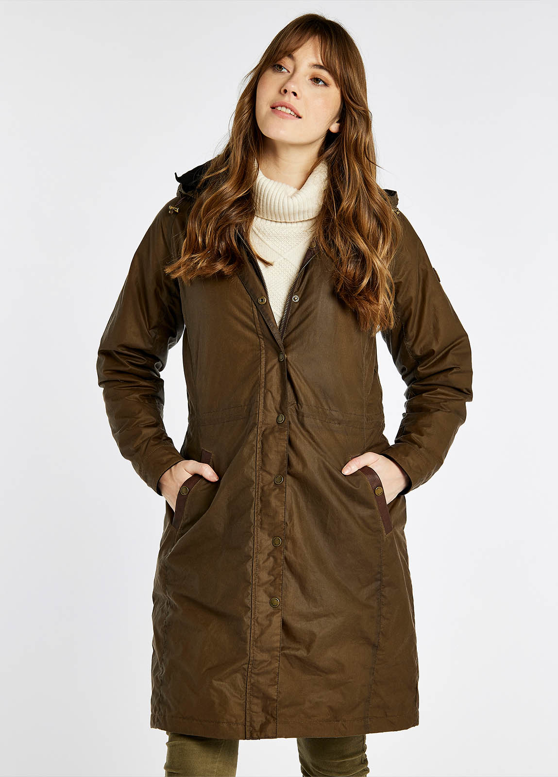 A female model wearing a ginger brown Dubarry Redington Wax coat, longer length coat with full zip. Model is wearing a light coloured jumper underneath. 